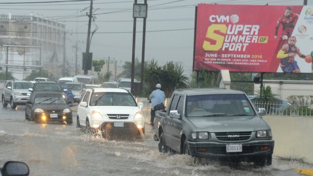 Cars drive along a street under heavy rain in downtown Kingston, Jamaica.