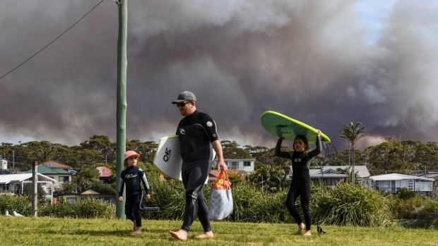 A bushfire rages behind holidaymakers at Currarong, looking south towards the fire.