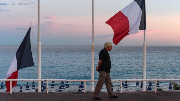 A man walks past French flags flying at half mast on the Promenade des Anglais in July.