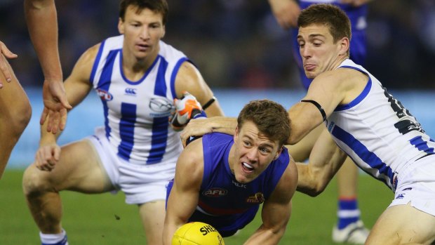 Jackson Macrae of the Bulldogs handballs away from Brent Harvey (left) and Shaun Atley of the Kangaroos.