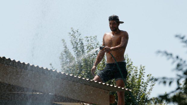 Wandin resident Ricky Booth hoses down his friend's roof to prevent ember attacks.