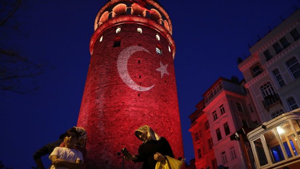 People take photos with their phones at the iconic Galata Tower, illuminated in Turkish flag colours, in Istanbul on Saturday.