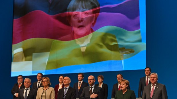 The board of Angela Merkel's Christian Democratic Union sings the national anthem in front of a screen showing the Chancellor. 