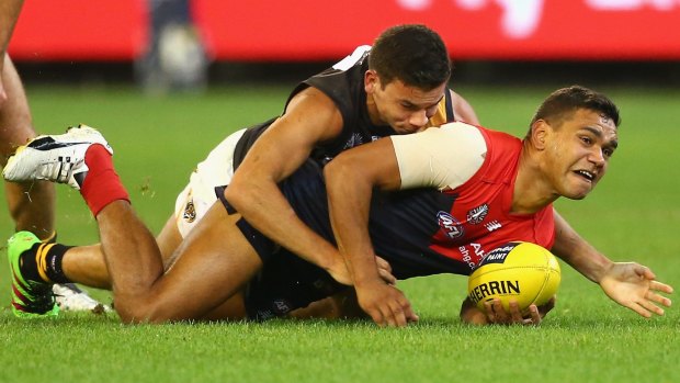 Neville Jetta of the Demons handballs as he is tackled by Daniel Rioli of the Tigers.