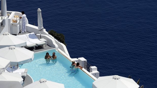 Tourists relax in a private swimming pool in the village of Oia on the Greek island of Santorini, Greece.