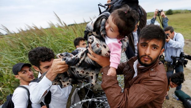 A Syrian man hands a child to another migrant over the Hungarian-Serbian border fence.