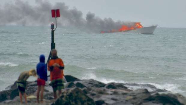 People stand on the shoreline as a tourist boat burns off Whakatane, New Zealand.  All 60 people on board were forced to jump into the sea to escape the flames.