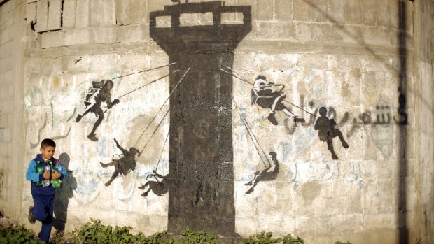A Palestinian child walks past a mural of children using an Israeli army watch tower as a swing ride, said to have been painted by British street artist Banksy, in the Gaza Strip town of Beit Hanoun.