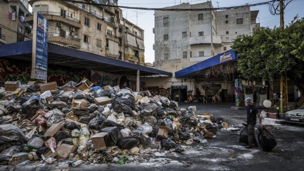 A restaurant worker takes bags of trash to add to a giant pile of garbage left uncollected for a week outside a bar named Floyd the Dog in Beirut.