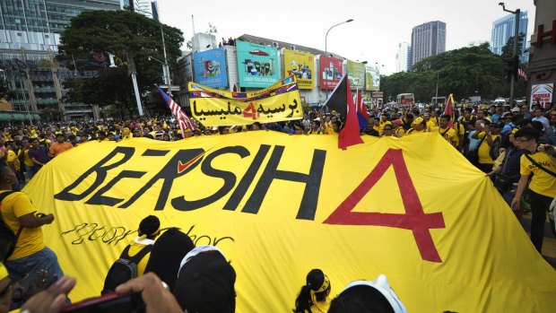Malaysian protestors unfold a banner reading 'BERSIH 4' while marching through the city streets.