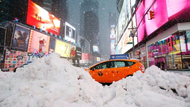 A taxi drives past piles of snow as a storm sweeps through Times Square on Tuesday.