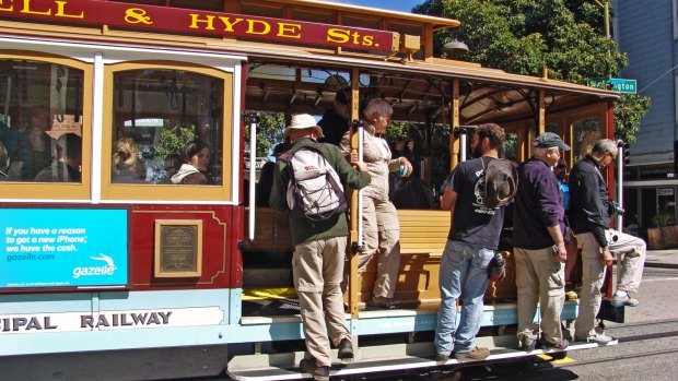 People and tourists travel on the side footboard of the famous cable car bus on a sunny September day in San Francisco.