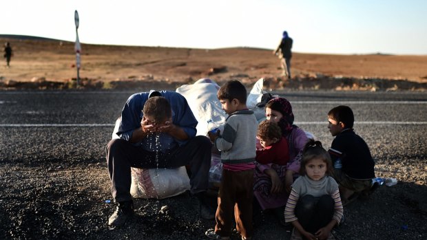 Kurdish refugees sit on the side of the road after fleeing Kobane.