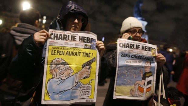 Women hold <i>Charlie Hebdo's</i> frontpages during a gathering on the Place de Republique.