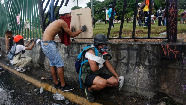 Demonstrators take cover next to the fence of La Carlota Air Base in Caracas, Venezuela.