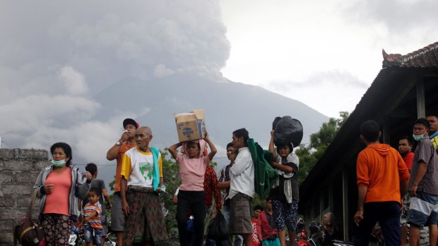 Villagers carry their belongings during an evacuation following the eruption of Mount Agung, seen in the background.