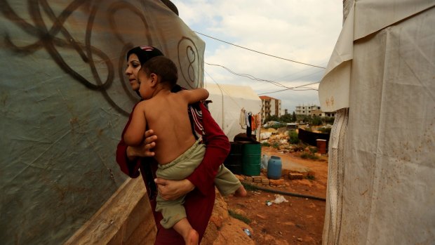 A Syrian refugee from Homs carries her child past makeshift homes in the unofficial refugee camp on the outskirts of Barsa, near Tripoli.