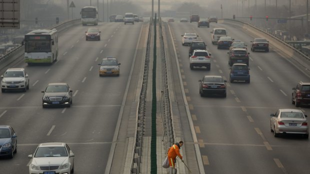 A road worker picks up trash along the median of a highway on a smoggy day in Beijing earlier this year. 