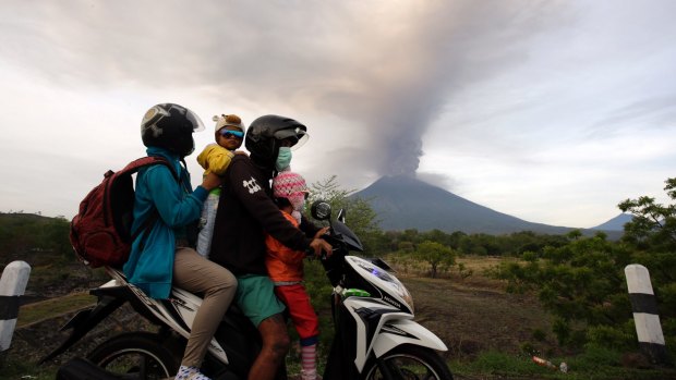 A family on a motorcycle passes by the Mount Agung volcano erupting in the background in Karangasem, Indonesia on Monday.