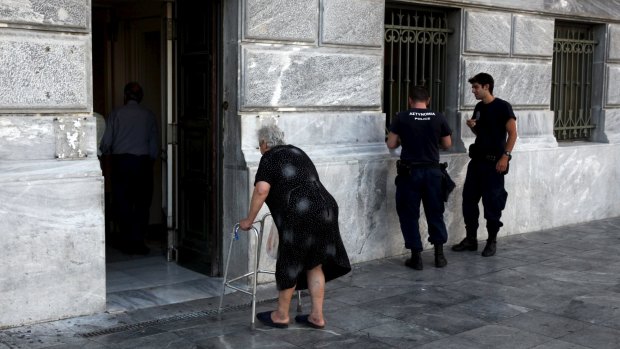 A pensioner arrives to receive part of her pension as police officers stand by at a National Bank branch in Athens on Tuesday. 