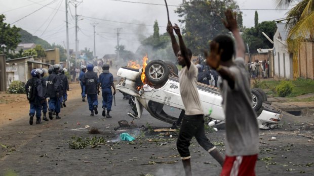 Riot police walk past a burning car destroyed by protestors in Bujumbura, Burundi.