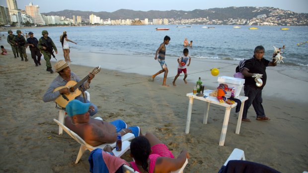 A roving seashell vendor walks past as a street musician serenades a local couple and marines along with local police patrol the shore of Papagayo Beach, Acapulco.