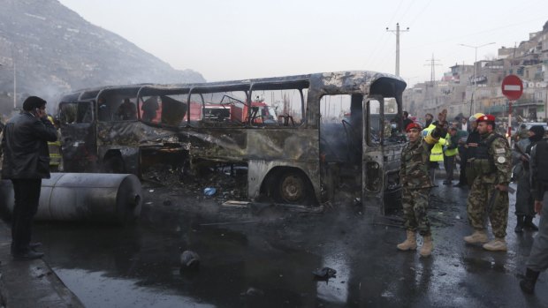 Afghan security guards inspect the damaged bus at the site of a suicide attack.