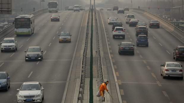 A road worker picks up rubbish along a highway on a smoggy day in Beijing.