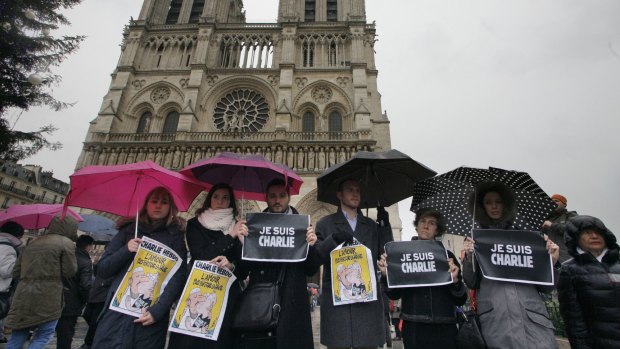 People hold signs reading '"e suis Charlie" (I am Charlie) as they stand under the rain with umbrellas in front of Notre-Dame Cathedral, where French Catholics celebrated a memorial Mass for the victims.