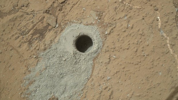 On the surface of Mars, a perfect circle is seen - the hole drilled by the rover Curiosity for its rock samples.