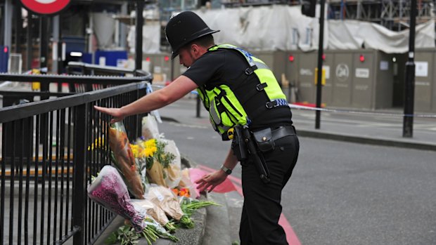 A police officer lays flowers passed to him by members of the public on the north side of London Bridge.