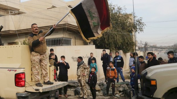 An Iraqi soldier waves the national flag as security forces patrol on the eastern side of Mosul, Iraq.