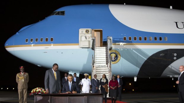 Kenyan President Uhuru Kenyatta, left, watches as President Barack Obama signs a guest book after arriving on Air Force One.
