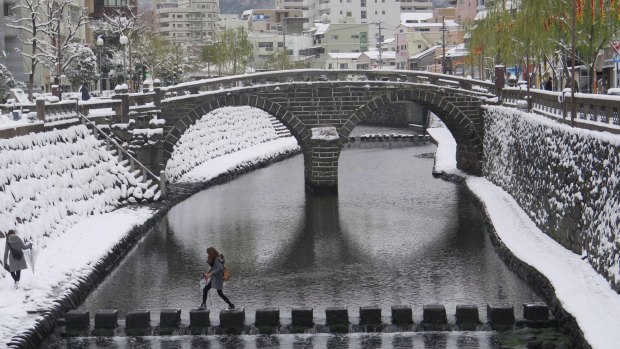 A woman walks on a step-stone bridge in front of Megane Bashi or the Spectacles Bridge, one of the oldest stone bridges in Japan, in snow-covered Nagasaki, southern Japan on Sunday.