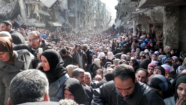 This picture taken by the UNRWA, shows residents of the besieged Palestinian camp of Yarmouk, queuing to receive food supplies, in Damascus, Syria in January 2014.