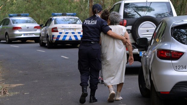A policewoman escorts an elderly woman being evacuated as a fire approaches Curral dos Romeiros, on the outskirts of Funchal.