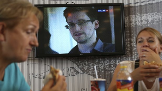 Passengers eat at a cafe with a TV screen showing a news program report on Snowden, in the background, at Sheremetyevo airport in Moscow.