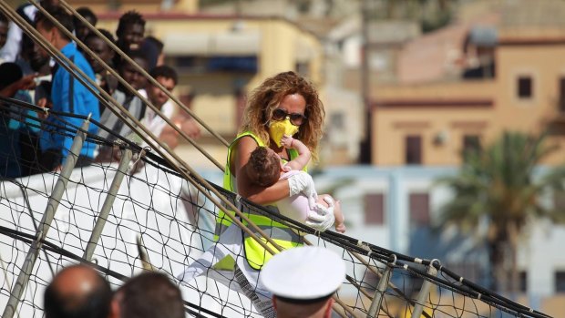 A migrant baby is disembarked from the Spanish ship Open Arms. Ten ships are estimated to be heading to Italian ports, while more than 7300 migrants have been saved off the coast of Libya over the past few days.