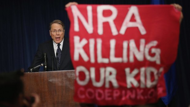 A demonstrator holds up a banner as NRA executive vice-president Wayne LaPierre speaks at a news conference after a popular assault-style rifle was used to slaughter 20 school children and six adults at Sandy Hook Elementary School in 2012.