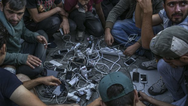 A group of migrants charge their phones using a TV station's generator outside the Keleti train station.