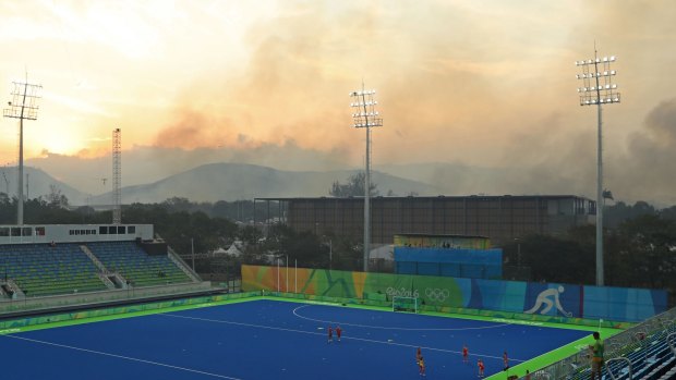 Athletes from Spain warm up on the pitch as a bushfire burns in the nearby hills of Deodoro before the quarter final hockey game against Great Britain in Rio on Monday.