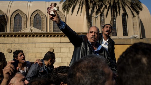A protester holds up a bloodied piece of rubble in the shape of a cross outside the church of St Peter and St Paul in the St Mark's Cathedral complex.