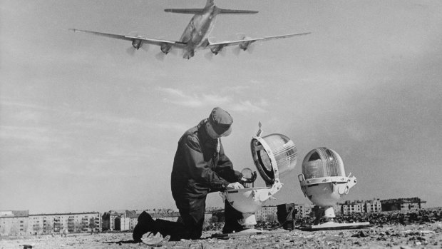 A technician mends the broken glass of a landing light at Tempelhof airport  as a Douglas C-54 Skymaster takes off during the Berlin Airlift, on April 25, 1949.