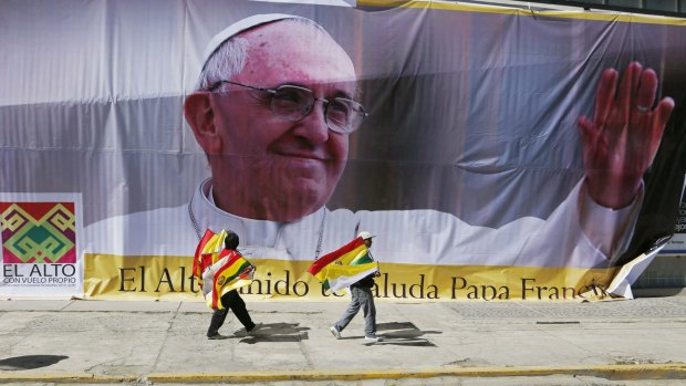 Street vendors selling Bolivian and Vatican flags pass a large image of Pope Francis ahead of the pope's arrival in El Alto, Bolivia, on Wednesday.