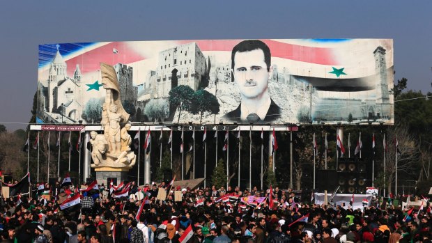 Pro-government supporters hold up the national Syrian flag and pictures of Syrian President Bashar al-Assad.