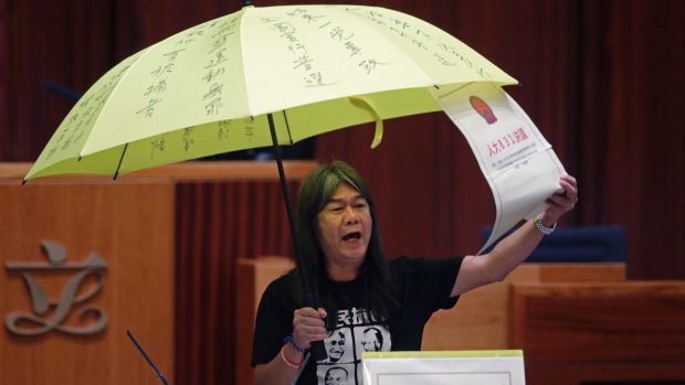 Elected pro-democracy lawmaker Leung Kwok-hung, known as "Long Hair," holds a yellow umbrella and a oversised mock copy of controversial, proposed anti-subversion legislation as he takes oath in the new legislature Council in Hong Kong.