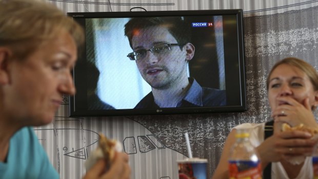 Passengers eat at a cafe with news report on Edward Snowden in the background at Sheremetyevo airport in Moscow in 2013.