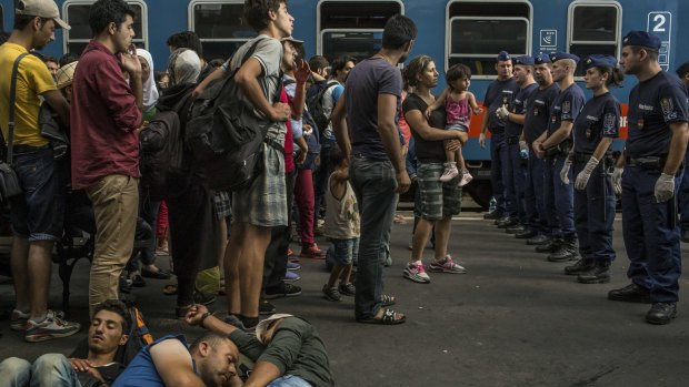 Police stand by as a few hundred people wait to take a train to Germany at the Keleti train station in Budapest.