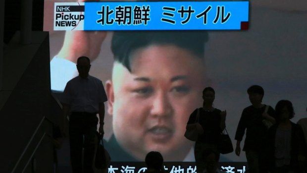 People walk past a giant TV screen showing North Korean leader Kim Jong-un celebrating the country's latest missile test launch. 