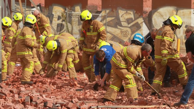 Firemen and workers with bare hands frantically dig into the fallen brick wall in Swanston Street in 2013.